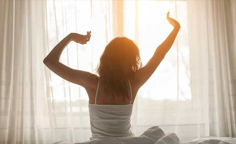 Woman stretching in bed with morning sunlight